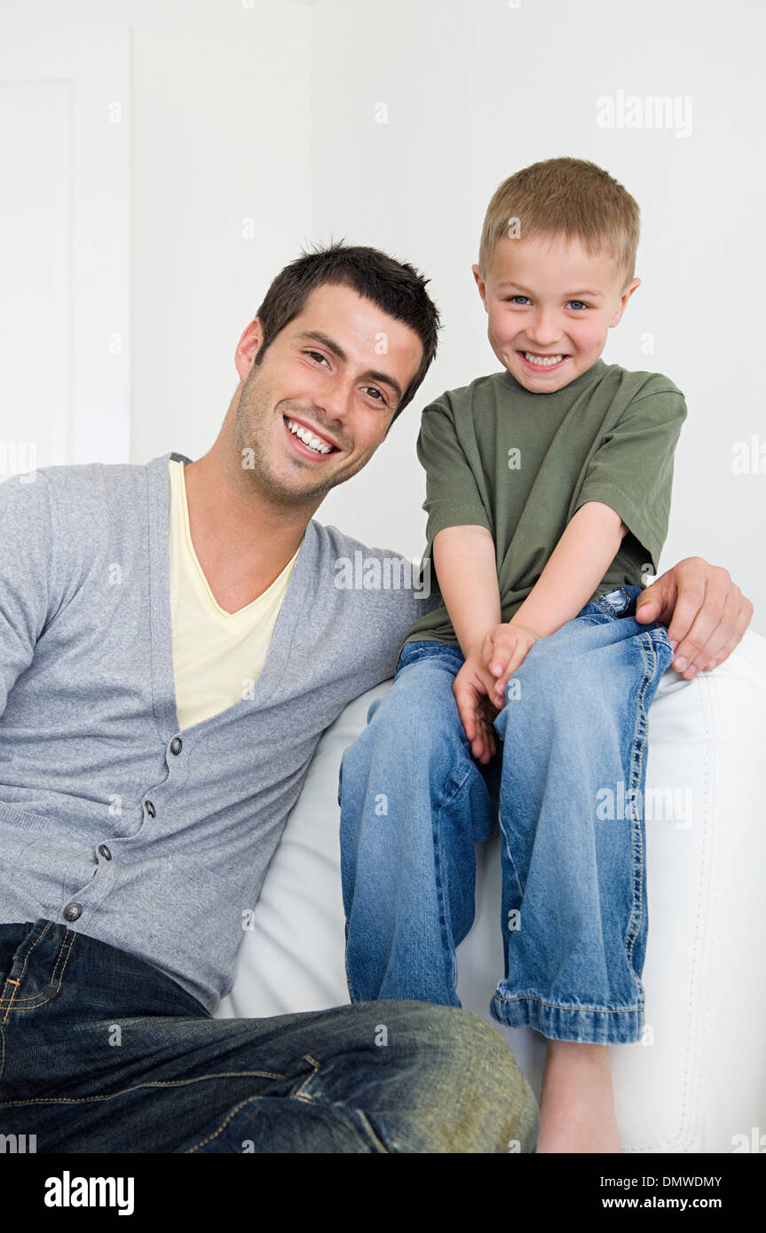 A man on a sofa beside a young boy wearing jeans. Stock Photo