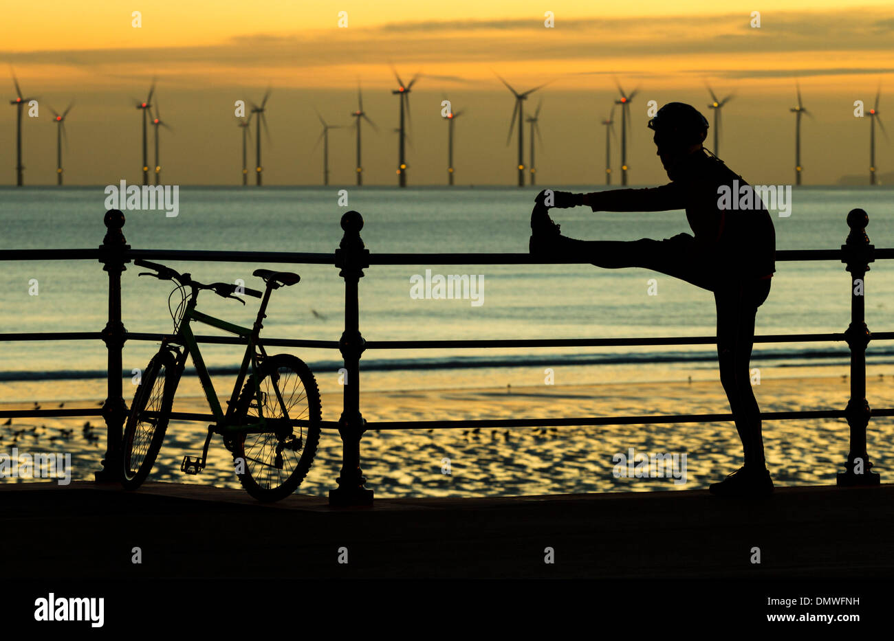 Mountain biker stretching at sunrise on Seaton Carew beach with Teesside Offshore Wind farm in background. UK Stock Photo