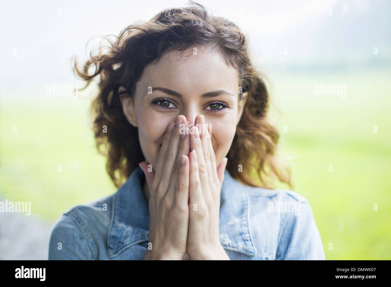 A young woman in a rural landscape with windblown curly hair. Covering her face with her hands and laughing. Stock Photo
