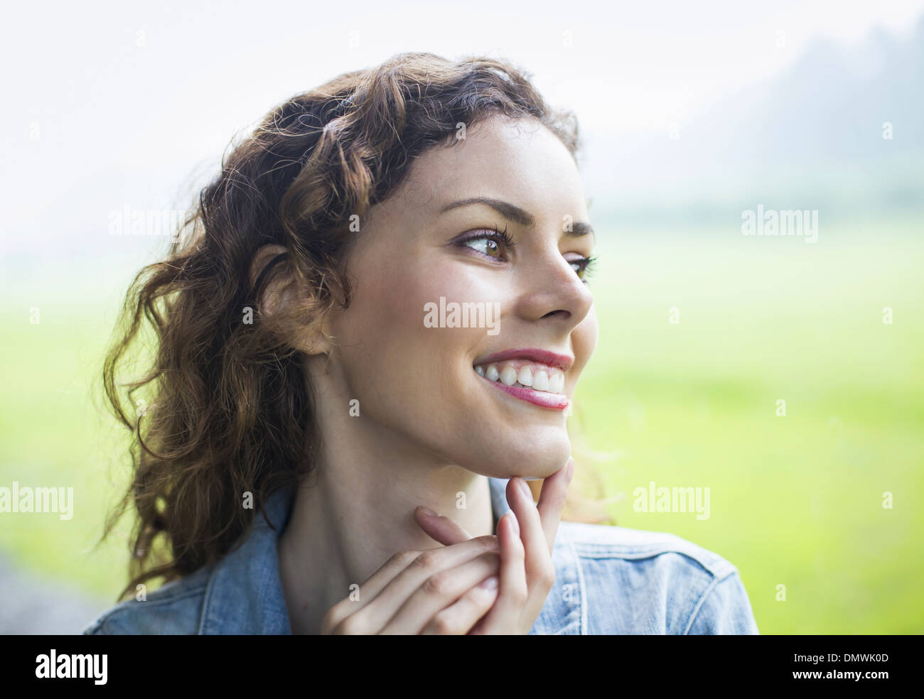 A young woman in a rural landscape with windblown curly hair. Looking away into  distance. Stock Photo