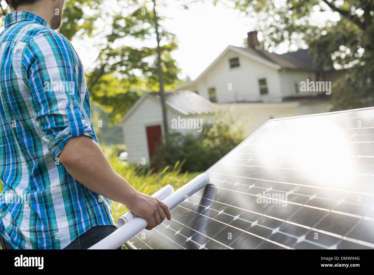 A man using a plan to place a solar panel in a farmhouse garden. Stock Photo