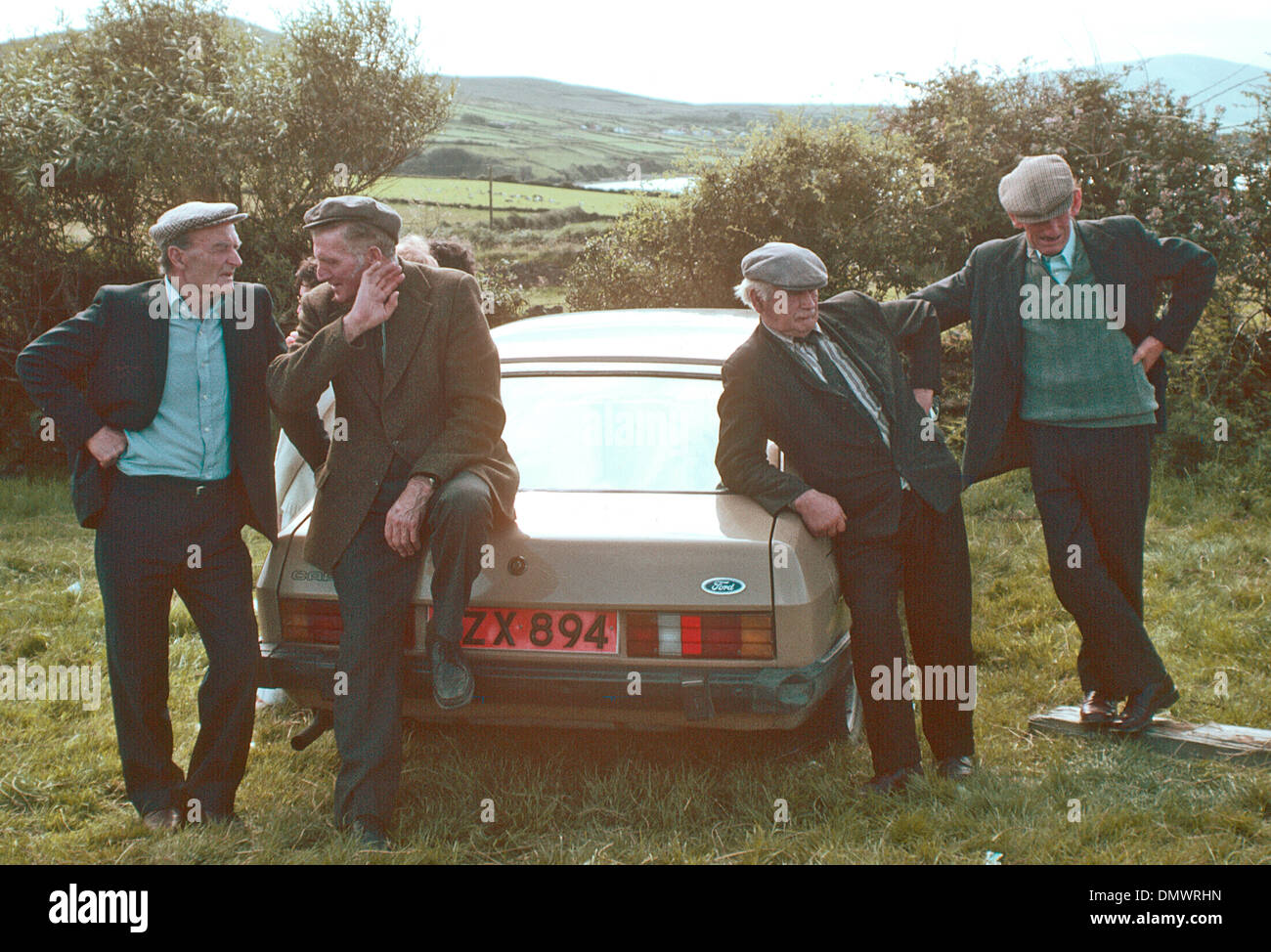 IRELAND Dingle Four farmers  in caps chat by a car 1970's Stock Photo