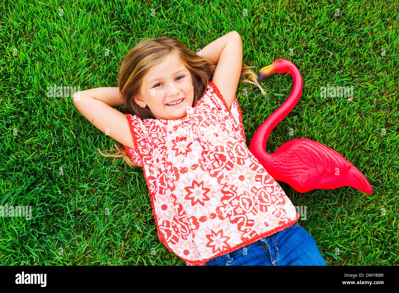 Smiling little girl lying on green grass with pink flamingo Stock Photo ...