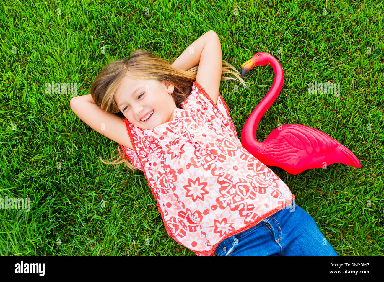Smiling little girl lying on green grass with pink flamingo Stock Photo ...