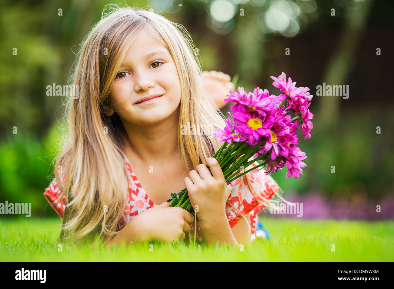 Portrait of a smiling little girl lying on green grass with flowers ...