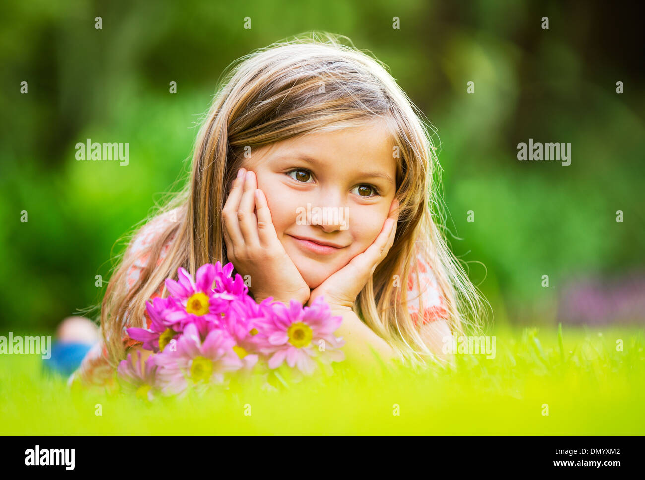 Portrait of a smiling little girl lying on green grass with flowers ...