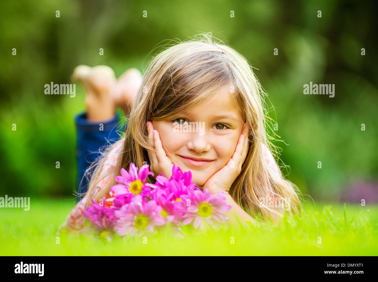 Portrait of a smiling little girl lying on green grass with flowers ...