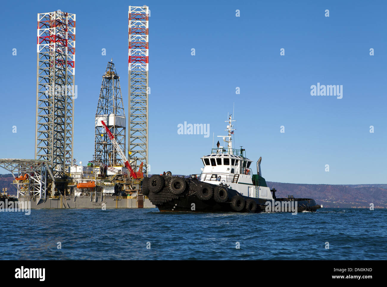 Oil drilling jack up rig with a tug boat in the Kachemak Bay near Homer Alaska on a sunny day. Stock Photo