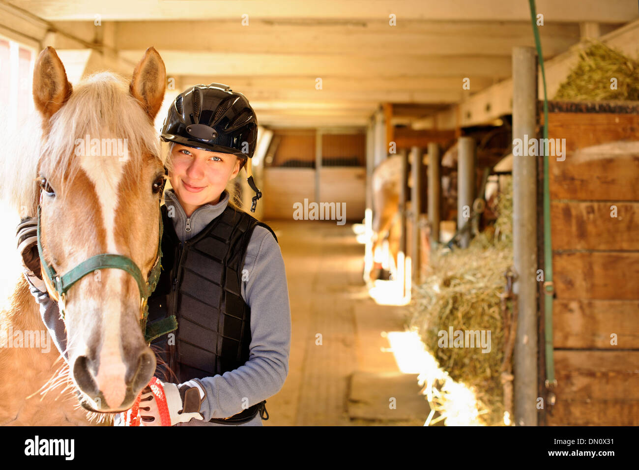 Young female rider with horse inside stable Stock Photo