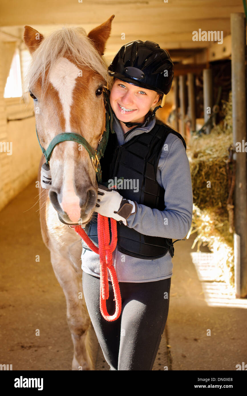 Young female rider with horse inside stable Stock Photo