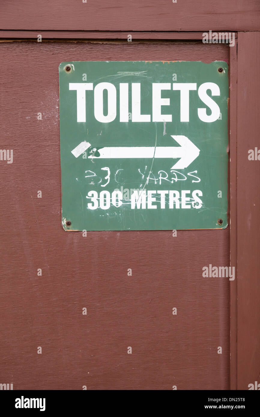 Sign for public toilets on wall giving distance in meters crossed out and  replaced with yards Stock Photo - Alamy
