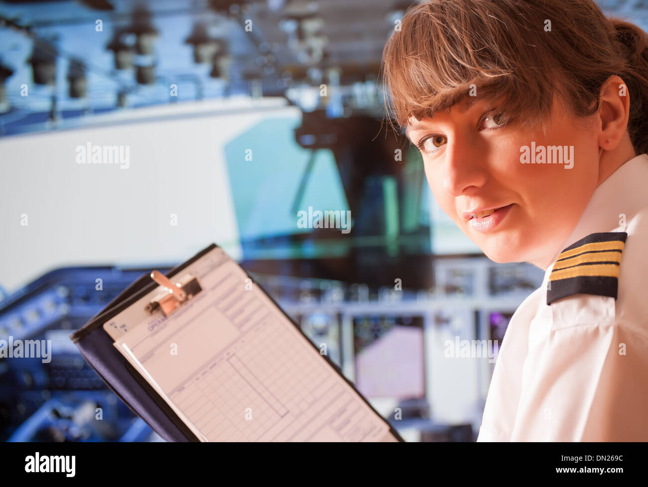 Beautiful woman pilot wearing uniform with epauletes and headset with notepad inside airliner Stock Photo