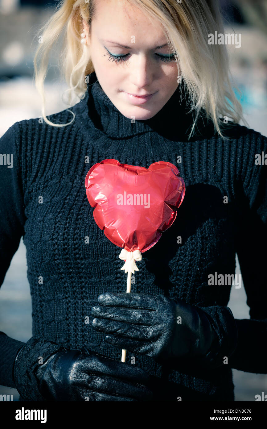 a blond girl is holding a heart shape balloon Stock Photo