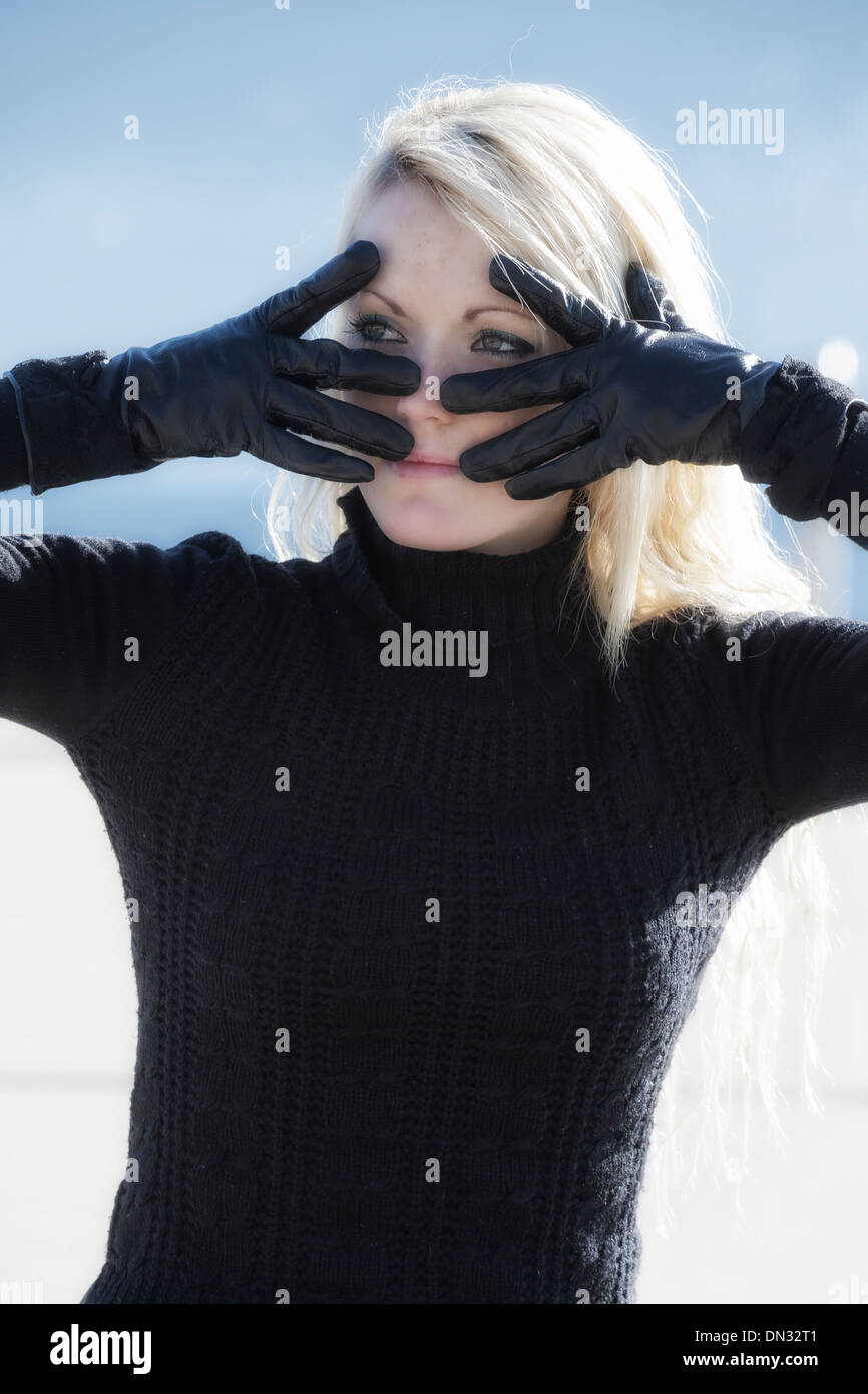 portrait of a beautiful young woman with long blond hair who is looking through black gloves Stock Photo