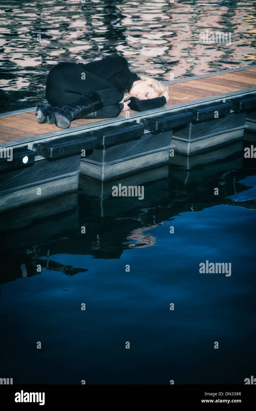 a woman in black clothes is lying on a jetty Stock Photo