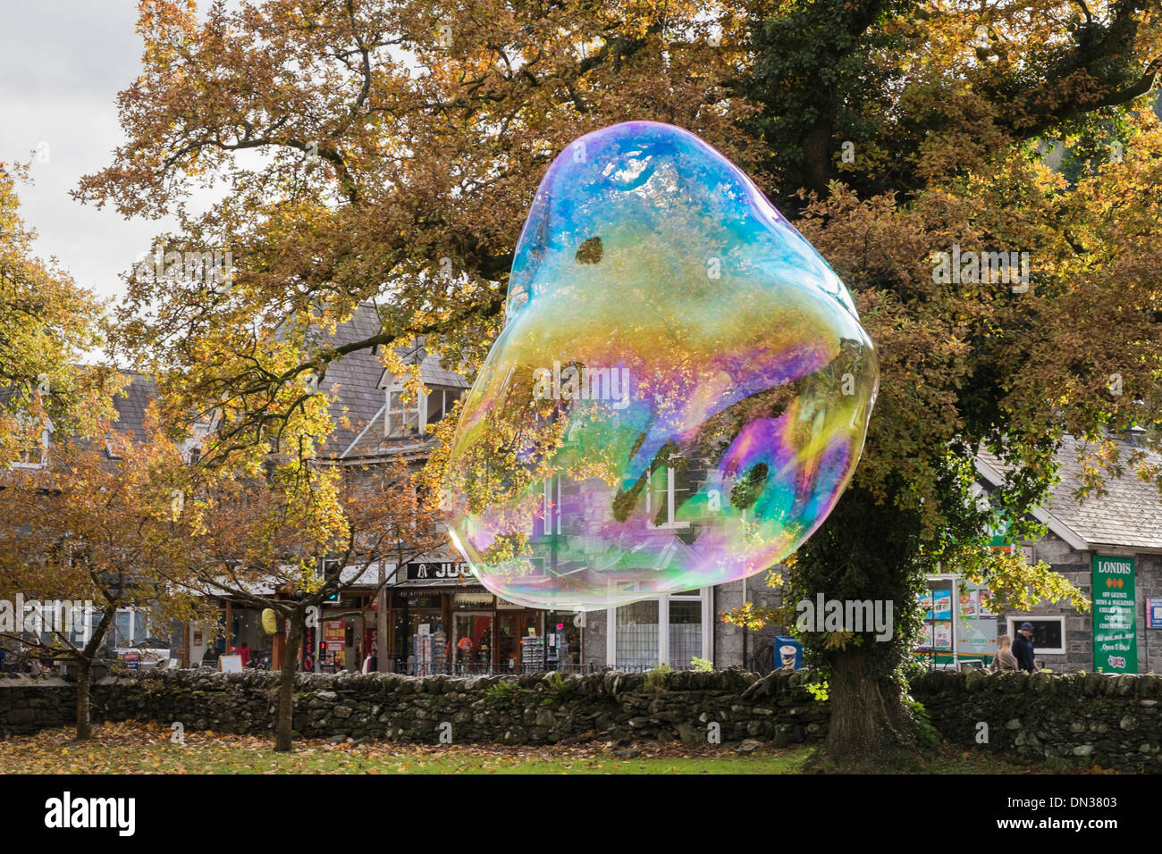 A giant soap bubble showing rainbow colours floats in air through Betws-y-Coed, Conwy, North Wales, UK, Britain Stock Photo