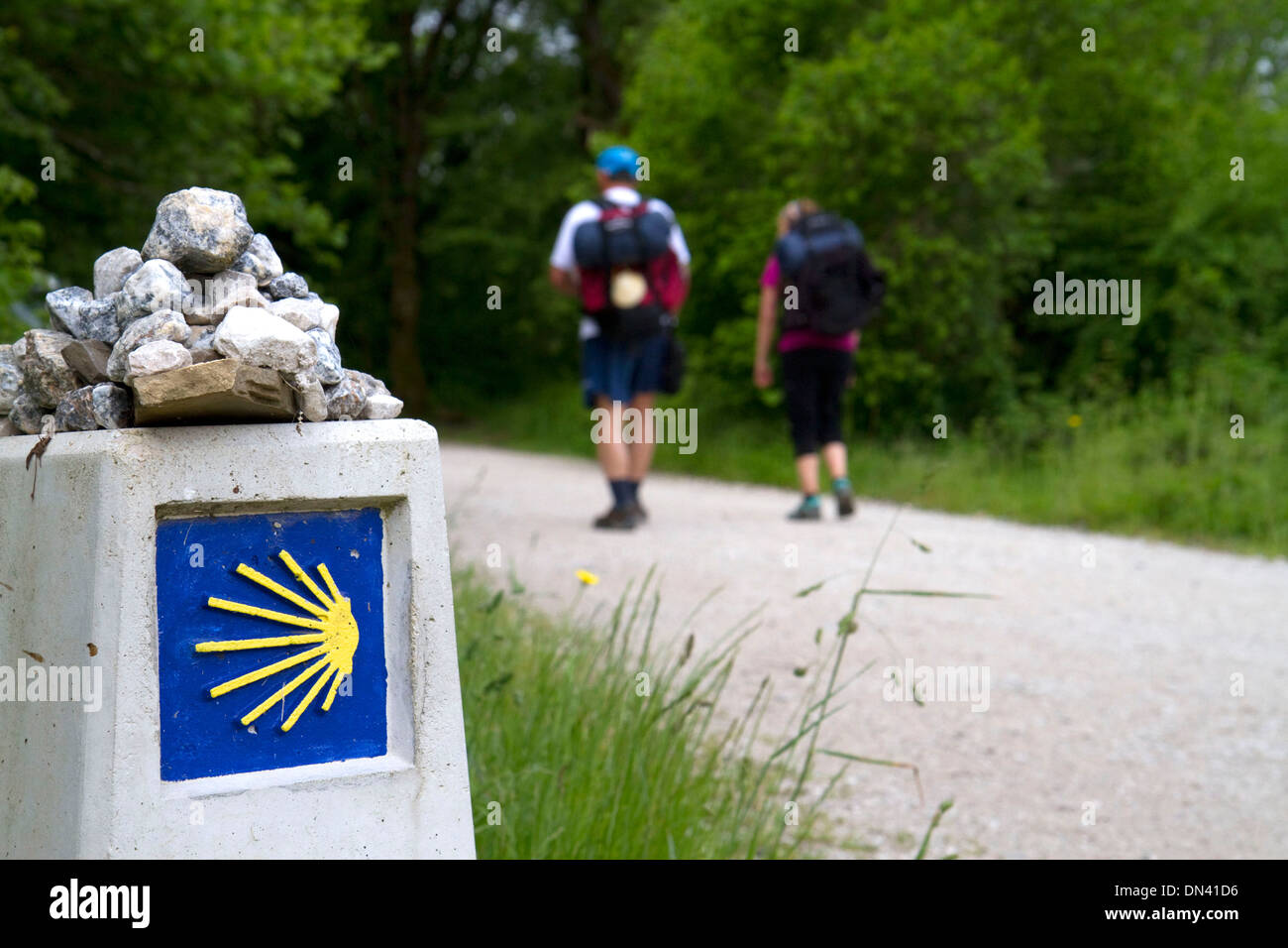 Pilgrims walk near a marker along the Camino De Santiago, the Way of St. James pilgrimage route, Navarra, Spain. Stock Photo