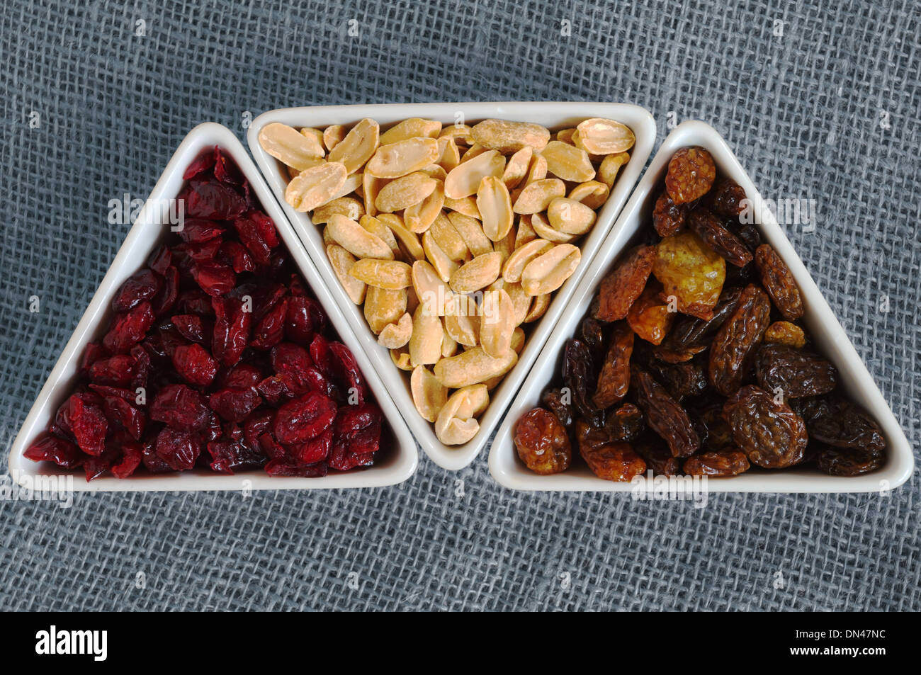 Dried cranberries, raisins and peanuts in three triangular bowls top view still life. Stock Photo
