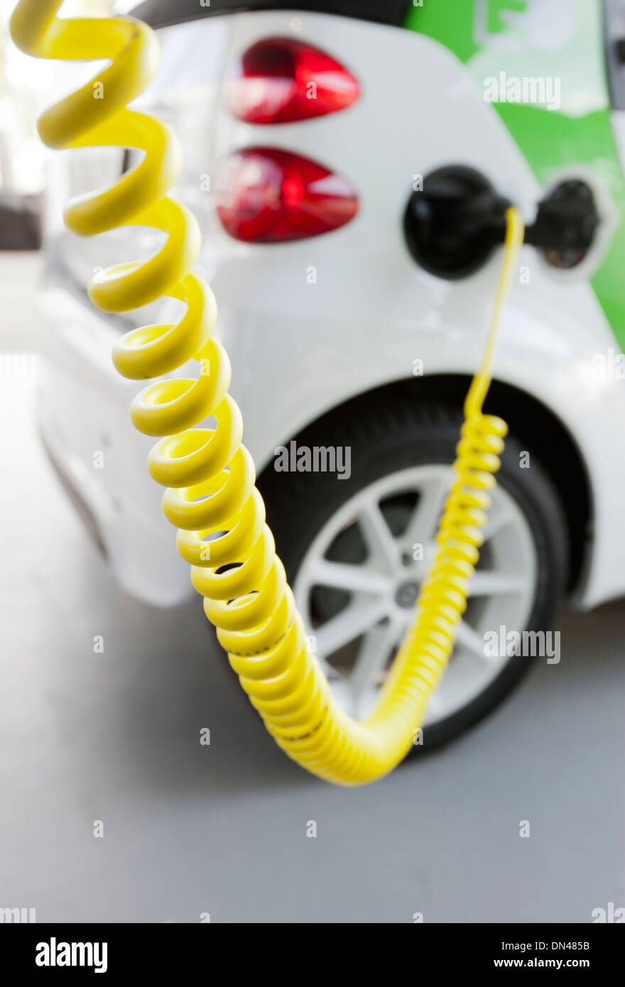 Electric vehile being charged on electric vehicle charging station. Bright yellow power line and plug in the foreground Stock Photo