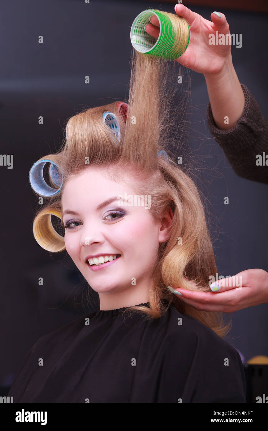 Beautiful young woman in beauty salon. Blond girl with hair curlers rollers by hairdresser. Hairstyle. Stock Photo