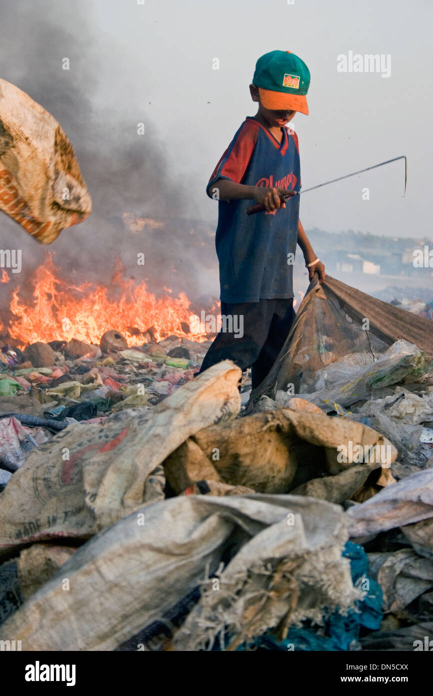 A child laborer boy is working near flaming piles of garbage at the polluted Stung Meanchey