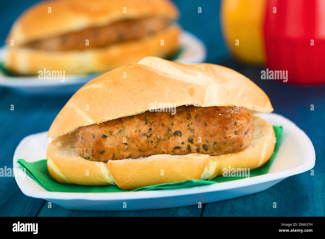 Fried bratwurst in bun, traditional German fast food served on disposable plate with napkin, ketchup and mustard in the back Stock Photo