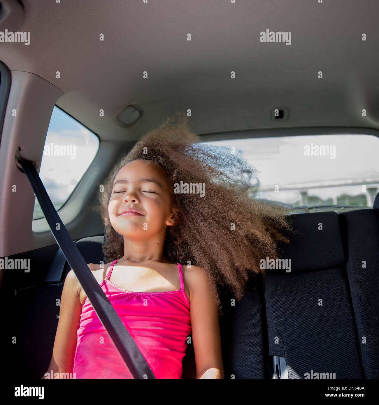 Mixed race girl enjoying wind in hair in back seat of car Stock Photo