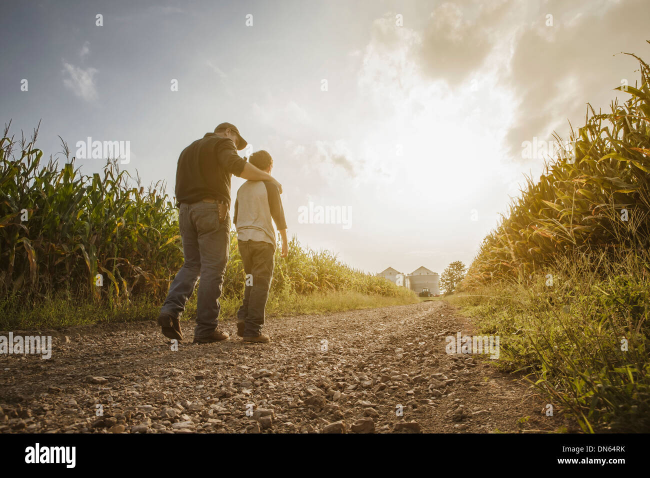 Caucasian father and son walking on dirt road through farm Stock Photo