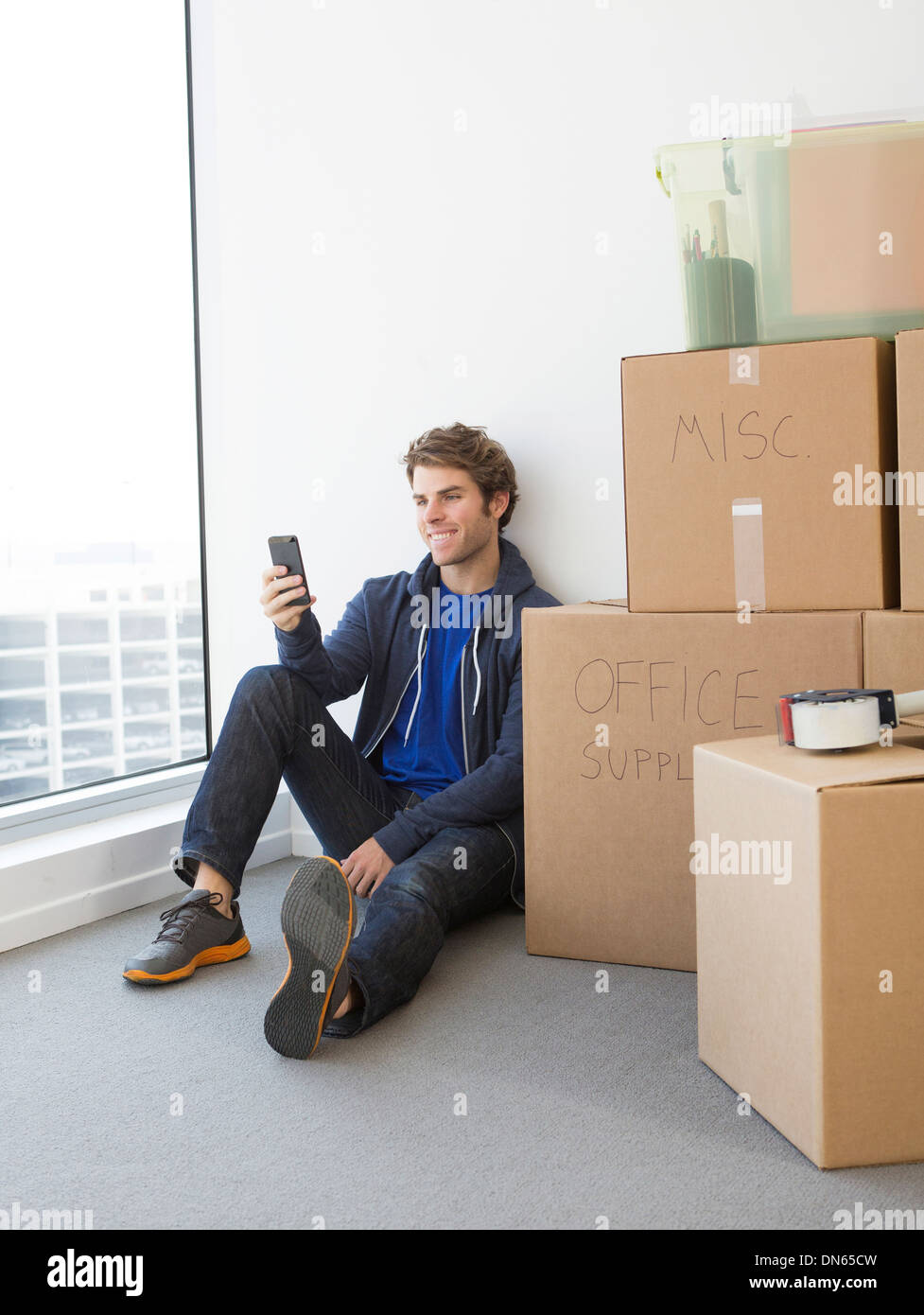 Man sitting amidst cardboard boxes on floor in living room of new house  stock photo