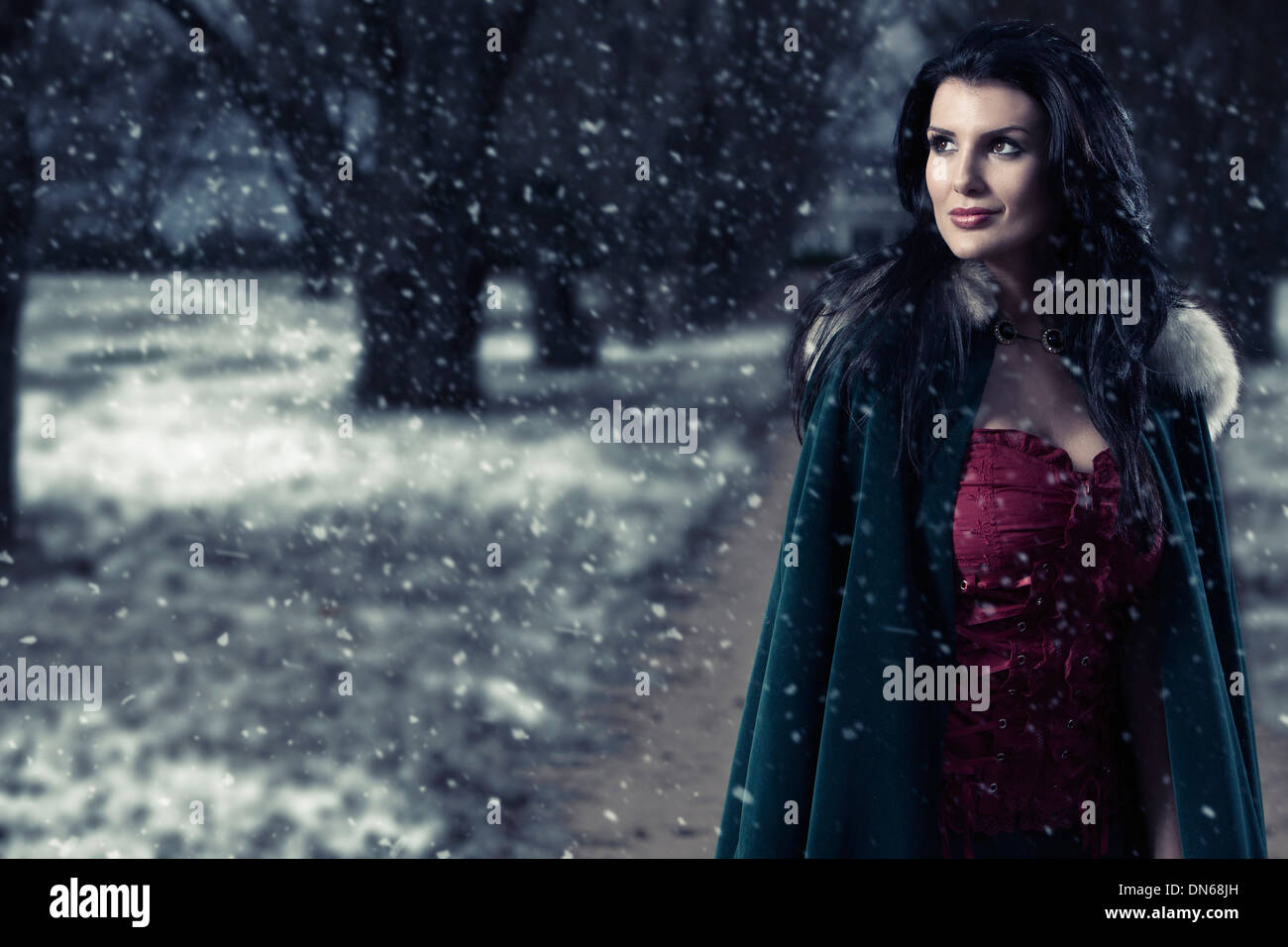 Woman in green cape walking down snowy path looking thoughtful and happy Stock Photo
