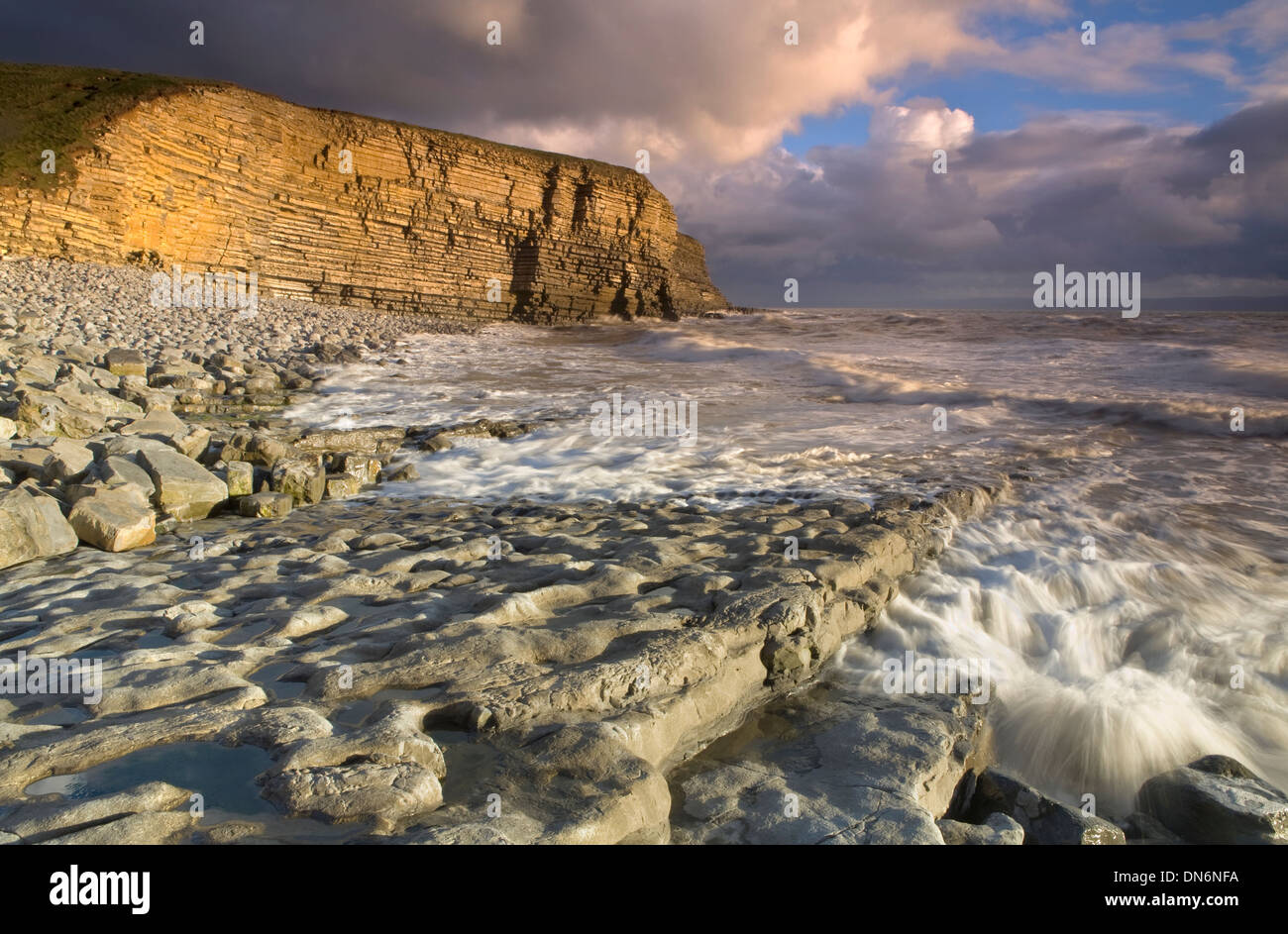 Strong sunlight lights up the cliffs at Nash Point, Vale of Glamorgan at sunset as the tide rolls in Stock Photo