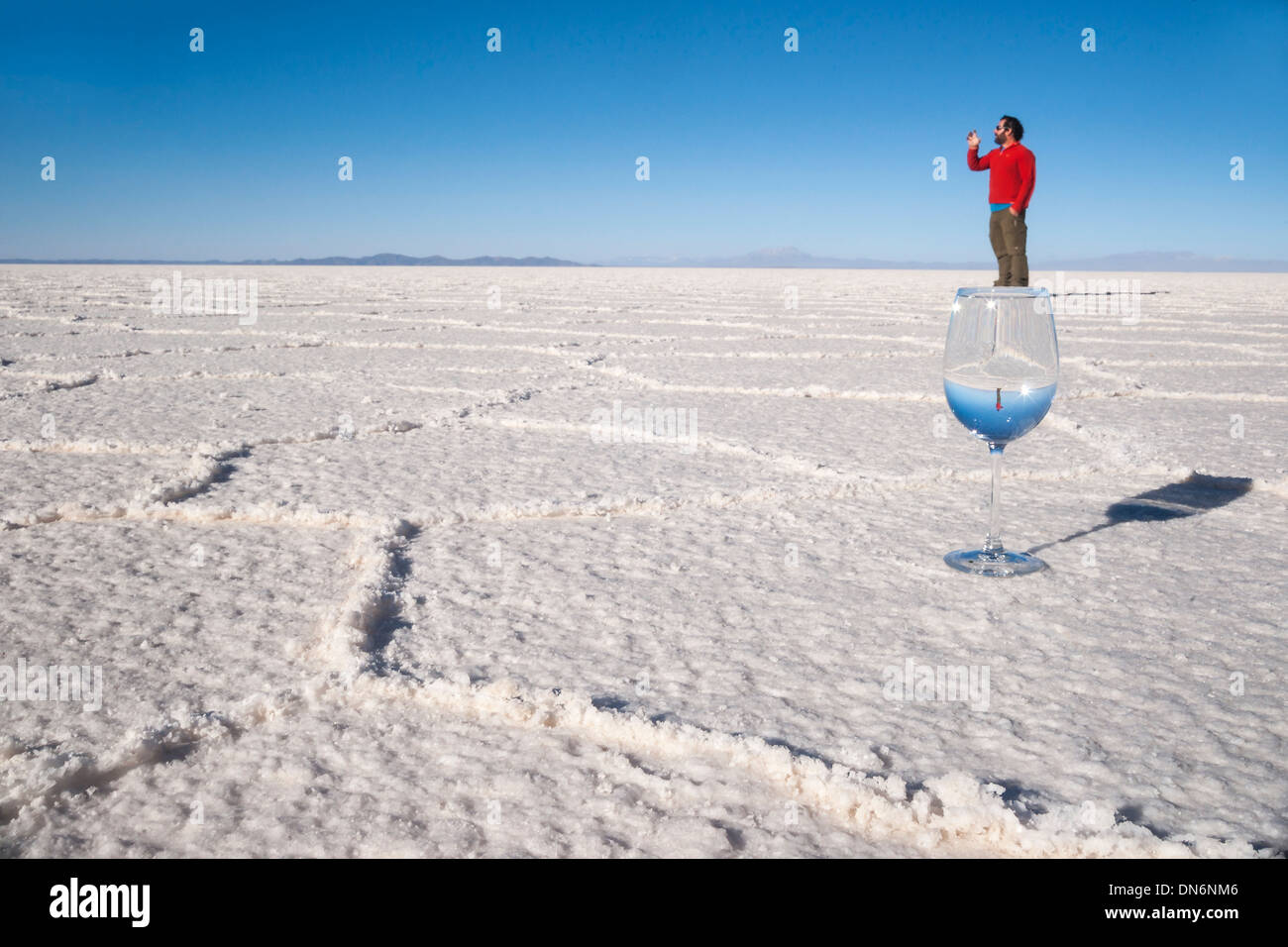 Perspective shot, a man balances on a wine glass on hexagonal shaped salt flats, Salar de Uyuni, Bolivia, South America Stock Photo