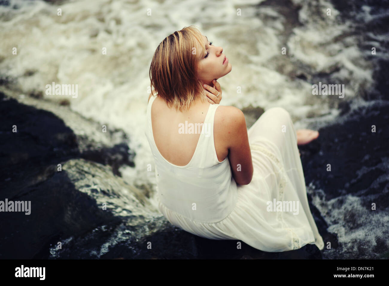 Young woman in white dress sitting on a creek Stock Photo