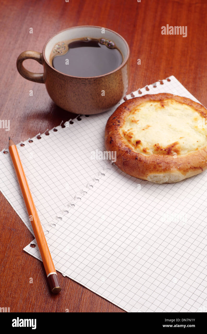 Sheet of paper, pencil, bun and coffee on the table Stock Photo