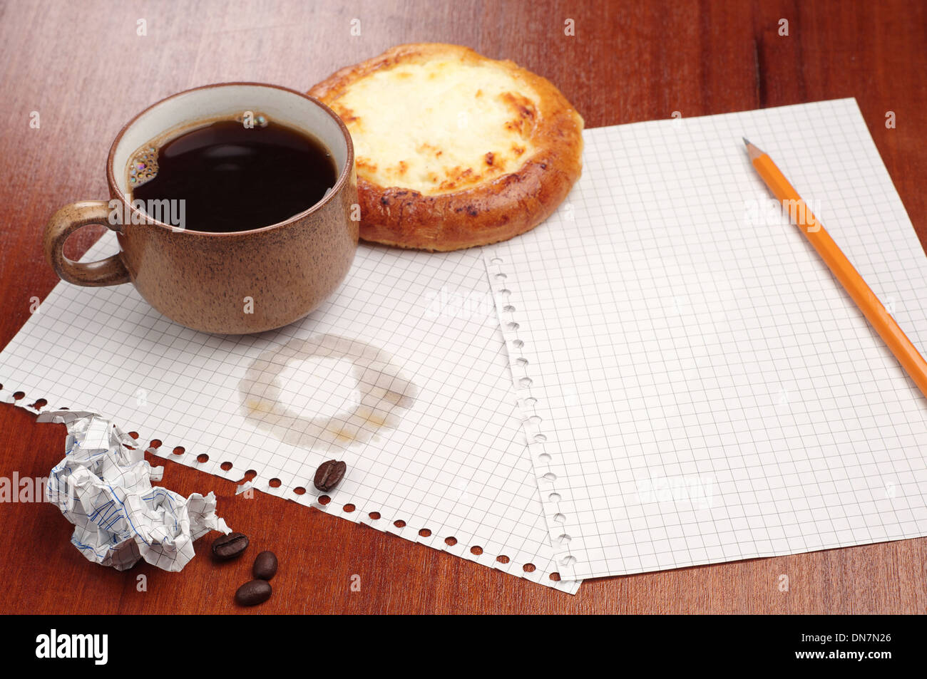 Cup of coffee with bun, pencil and crumpled paper on the table Stock Photo