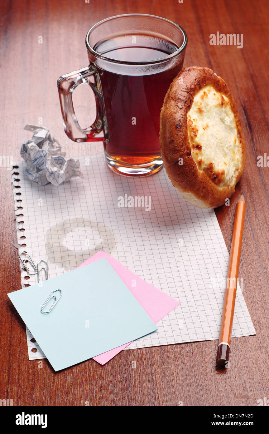 Notebook paper, pencil and a cup of tea with bun on the table Stock Photo
