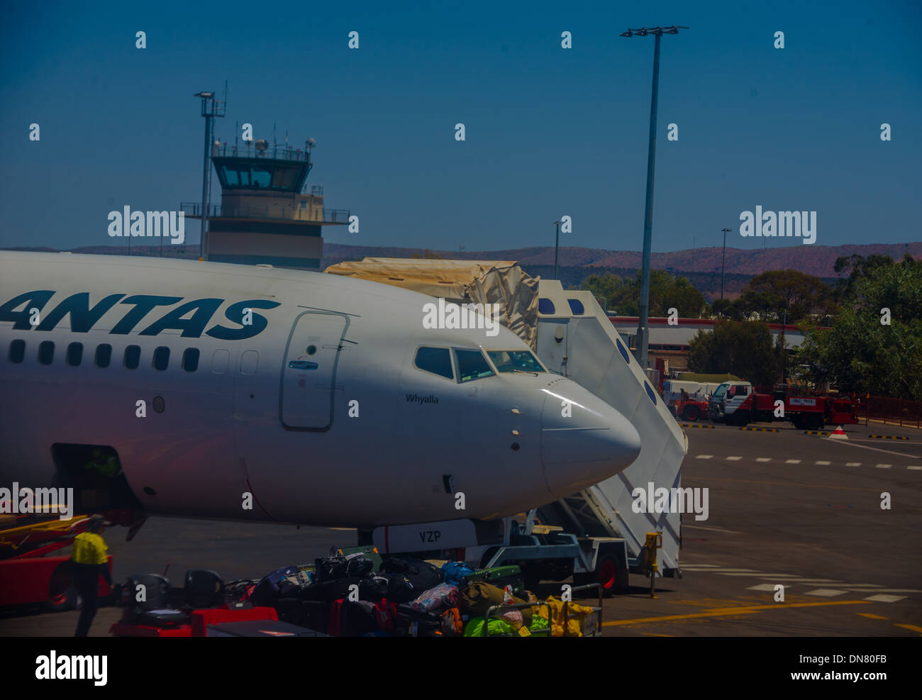 Qantas plane on tarmac with red centre background at Alice Springs baggage handler on tarmac loading airplane flight steps Stock Photo