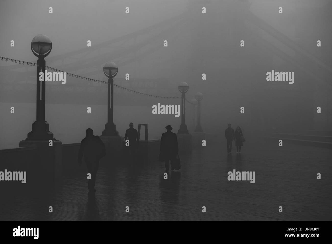 Silhouetted figures, including a man in a hat, walking against the foggy backdrop of the Thames by Tower Bridge Stock Photo