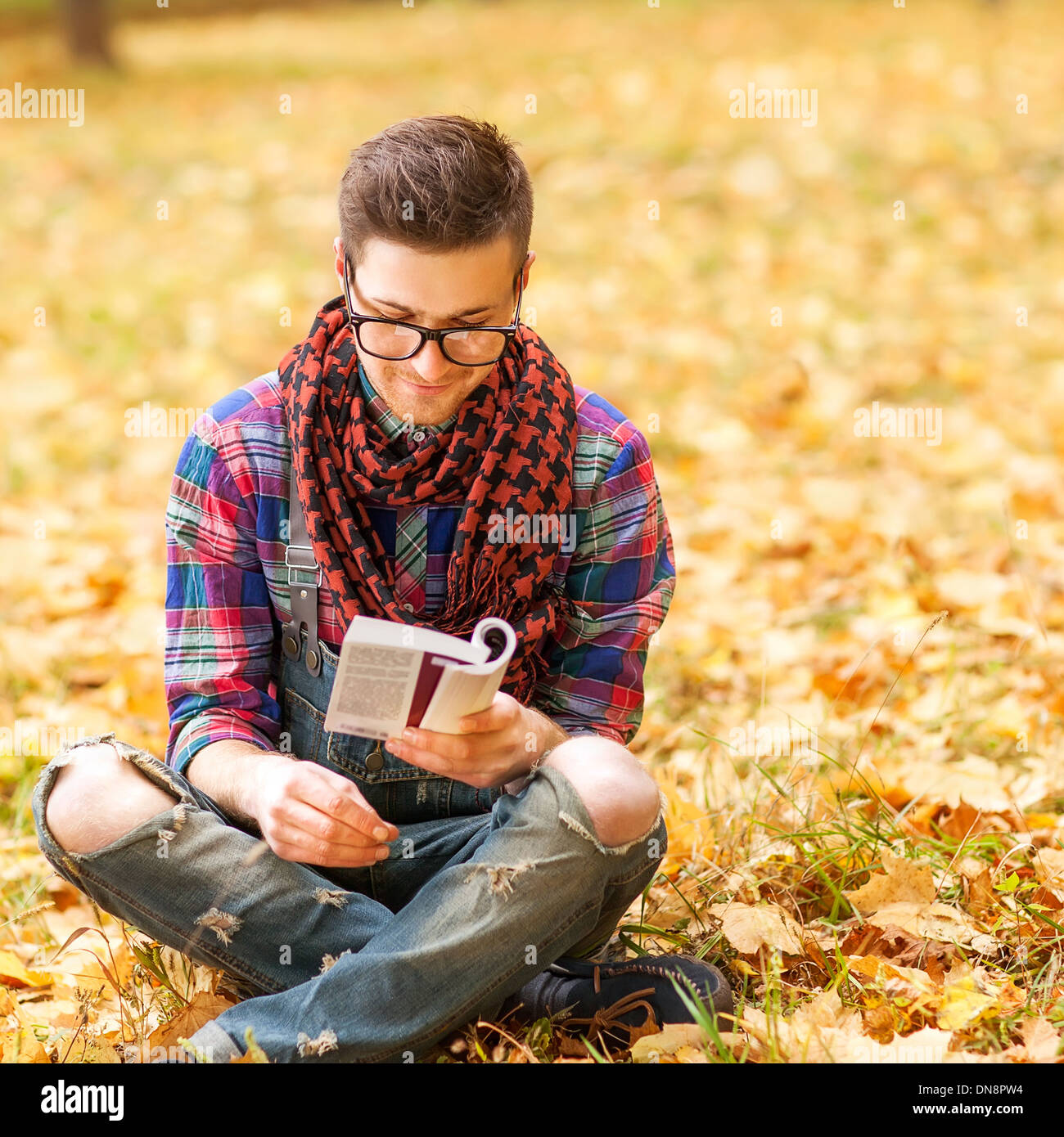 Young hipster relaxed man reading book in nature, back on tree, meadow behind Stock Photo