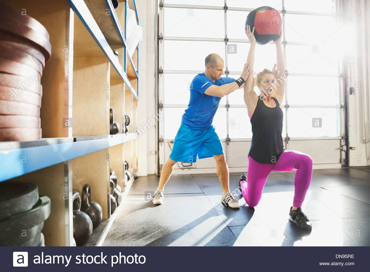Gym instructor assisting woman with medicine ball lunge Stock Photo