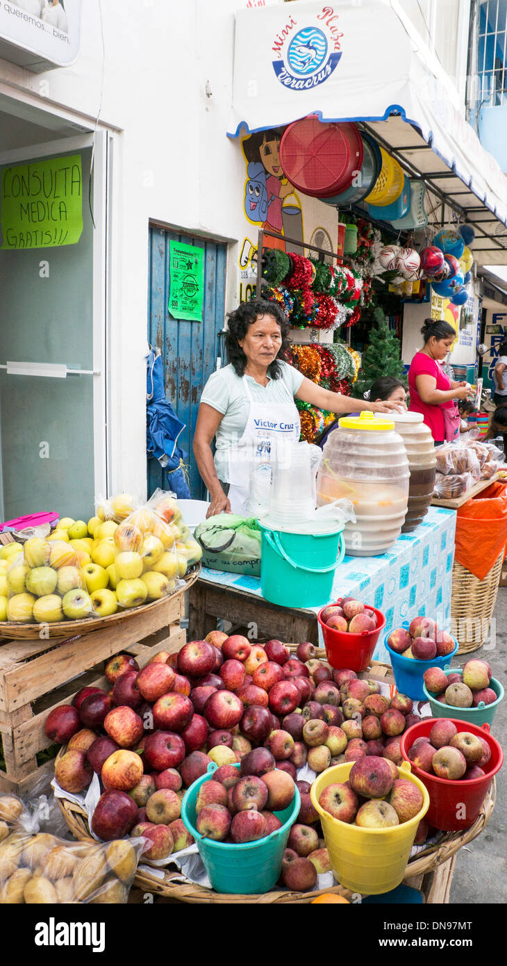 market day stalls line main street as Mexican woman vendor sells agua de fruta fruit water with apples heaped in foreground Stock Photo