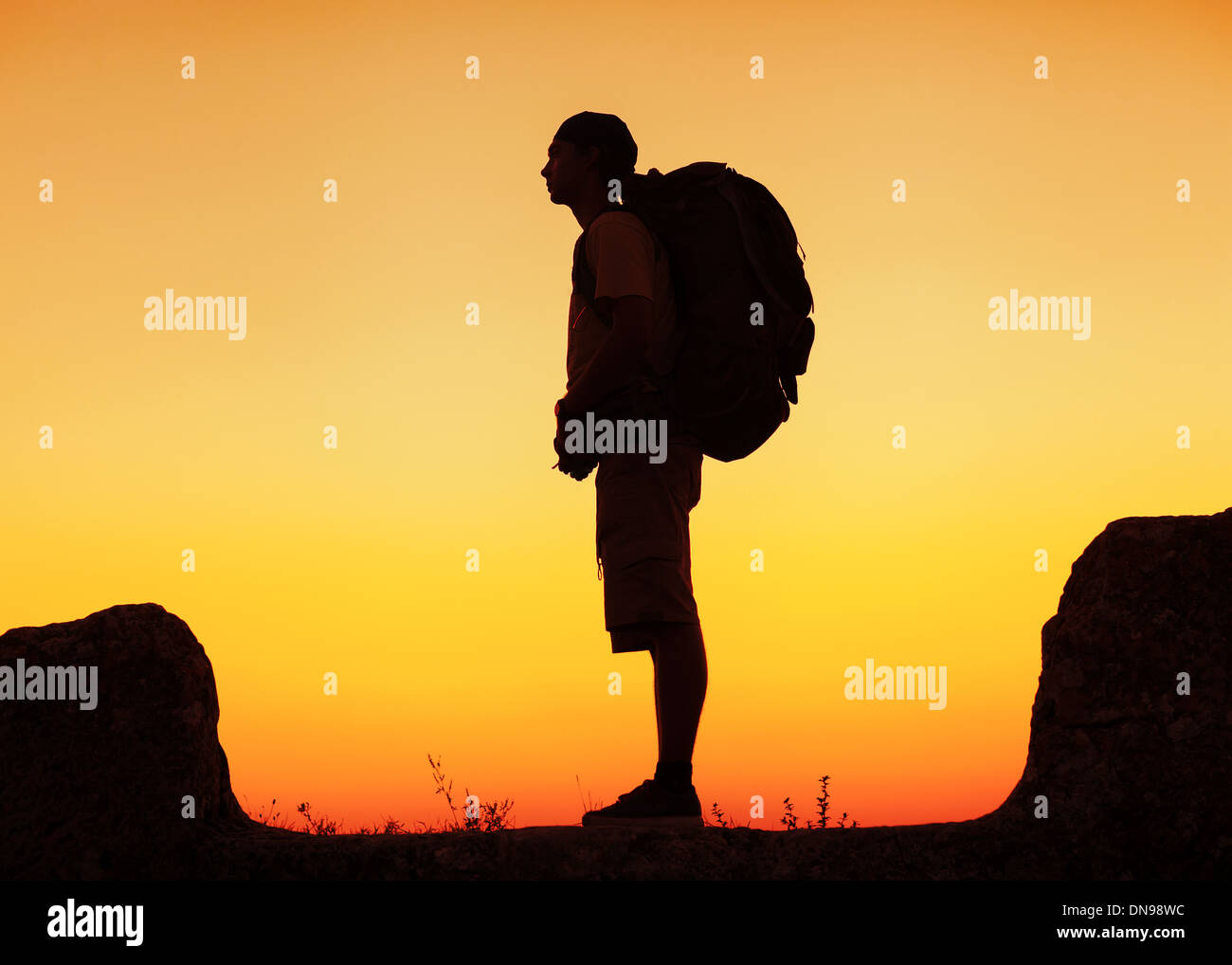 Hiker with backpack standing on top of a mountain and enjoying sunset ...