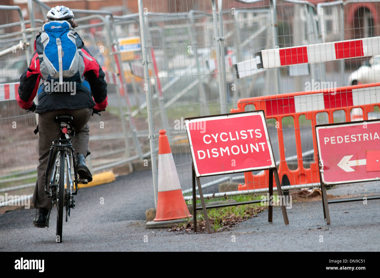 Cyclist on pavement riding past 'cyclist dismount' sign at roadworks Stock Photo