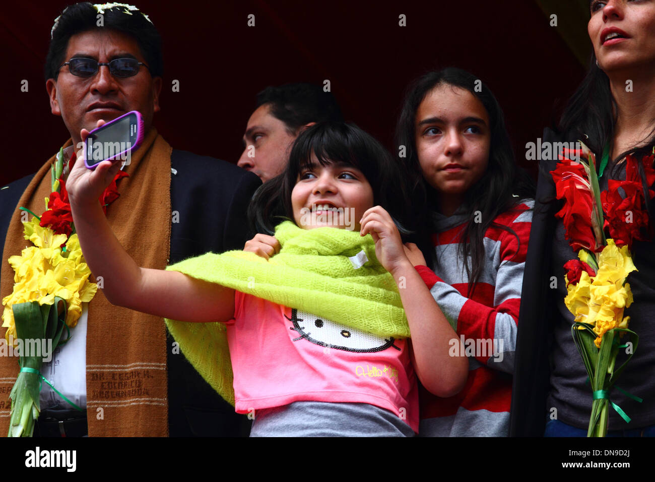 La Paz, Bolivia. 20th Dec, 2013. The daughter of president of the Bolivian Senate Gabriela Montaño (who is standing far right) takes a photo while watching the launch of Bolivia's first communications satellite as it is transmitted live from the XiChang space station in China. The Tupac Katari satellite has been built at a cost of around $300million. Standing left wearing a brown scarf is the Prefect of La Paz department, Cesar Cocarico. Credit:  James Brunker / Alamy Live News Stock Photo