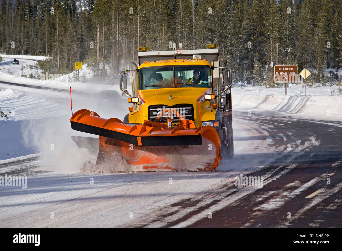 A snow plow and sanding truck clears a mountain highway of snow