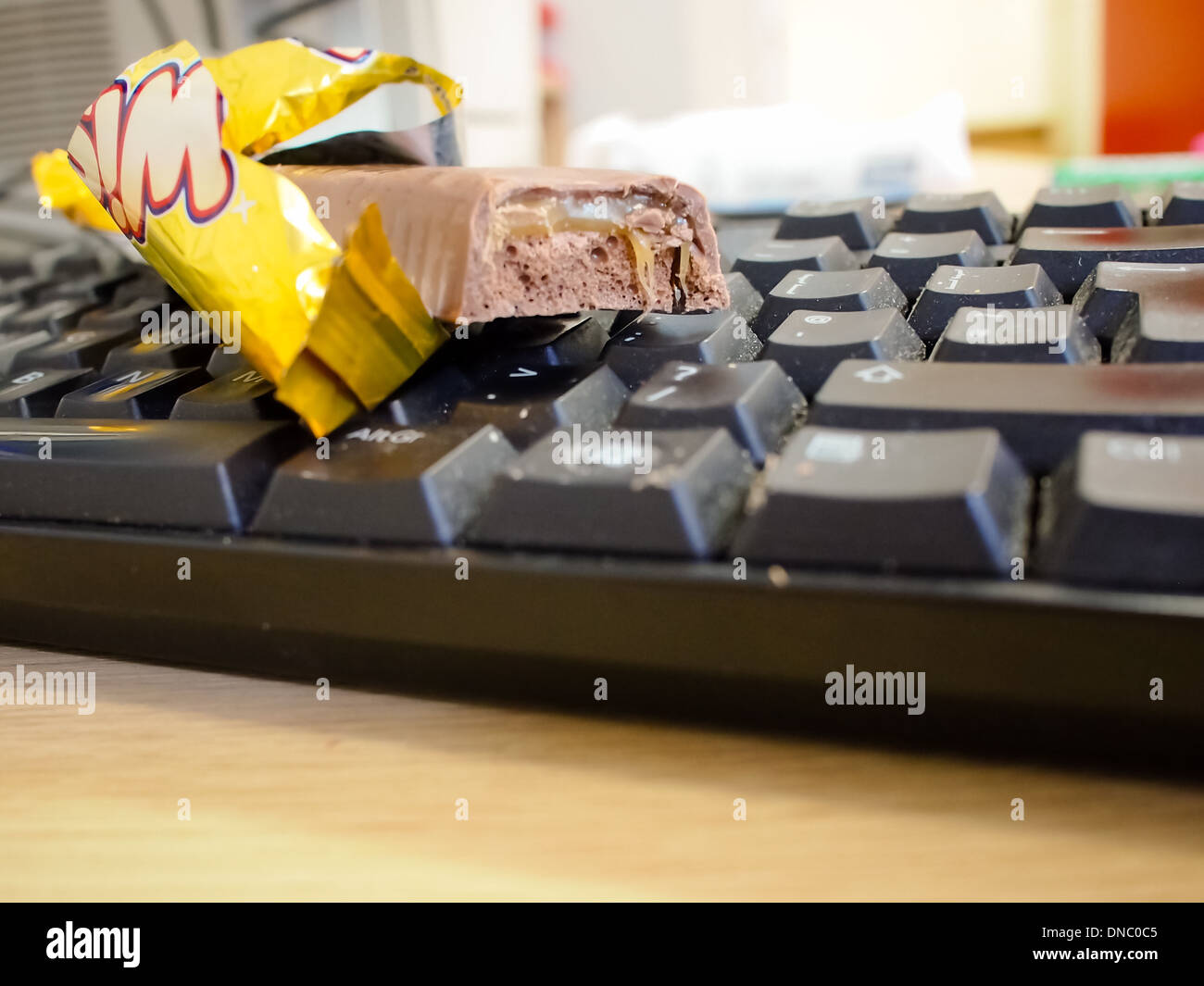 A bar of chocolate resting on a computer keyboard with food crumbs on