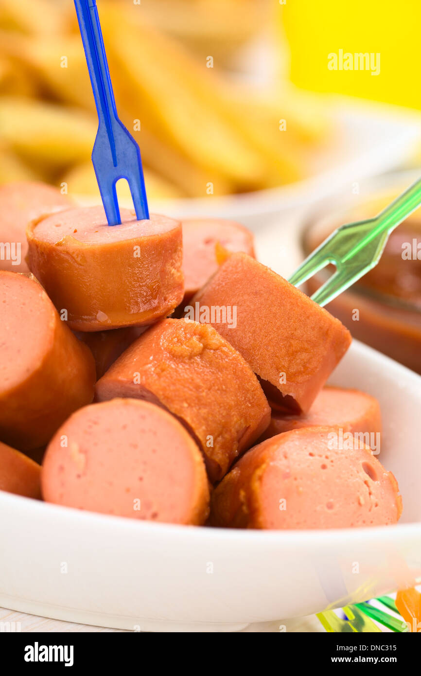 Fried sausage pieces with two small plastic forks, French fries and ketchup in the back Stock Photo