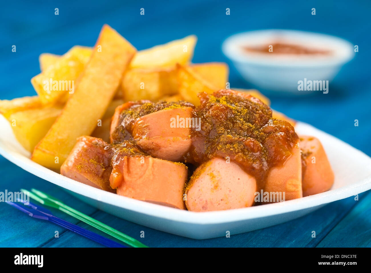 German fast food called Currywurst served with French fries on a disposable plate with party forks in the front Stock Photo