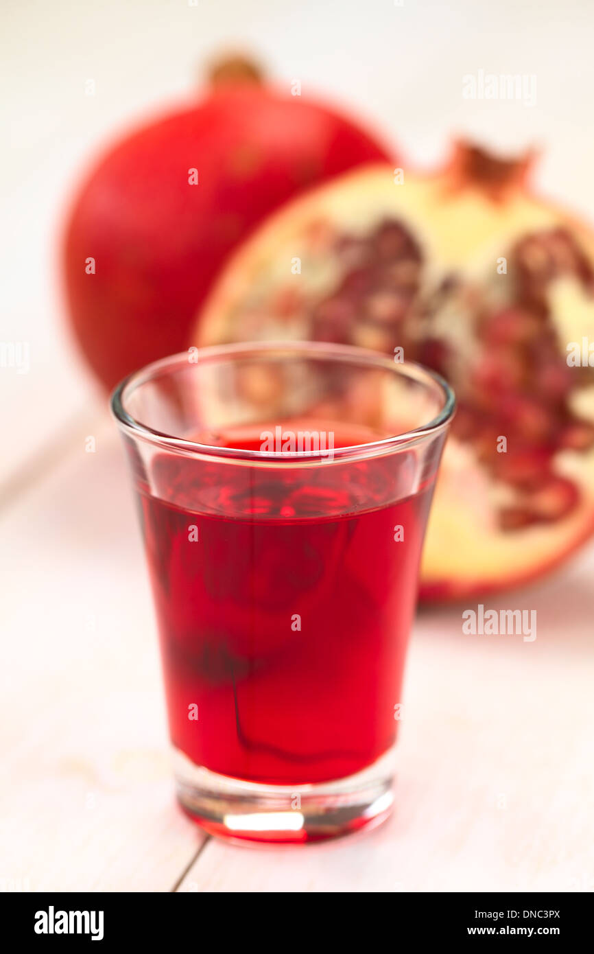 Grenadine syrup in shot glass with pomegranate in the back (Selective Focus, Focus on the front rim of the glass) Stock Photo