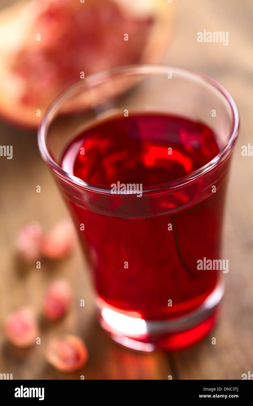 Grenadine syrup in shot glass with pomegranate seeds on the side and pomegranate in the back Stock Photo